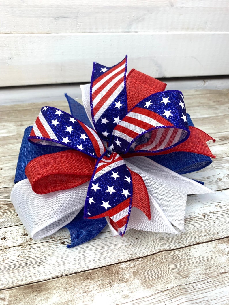 May include: A red, white, and blue bow with a star pattern. The bow is made of ribbon and mesh and is perfect for a patriotic display.