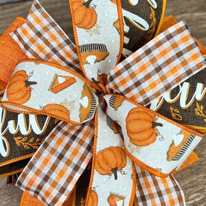 Op de afbeelding: Een herfstthema strik met oranje, bruin en wit geruit lint, een bruin lint met het woord "dankbaar" in wit, en een wit lint met oranje pompoenen en taartontwerpen.