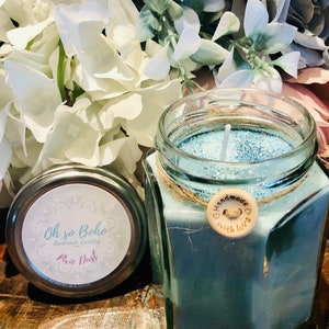 May include: A blue candle in a glass jar with a silver lid. The jar has a rustic twine bow and a small wooden tag that says "Handmade with love". The candle is labelled "Oh so Boho Handmade Candles Pixie Dust".