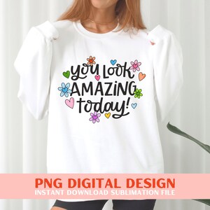 May include: White sweatshirt with the text "you look amazing today!" in black script with colourful flowers and hearts surrounding the text.