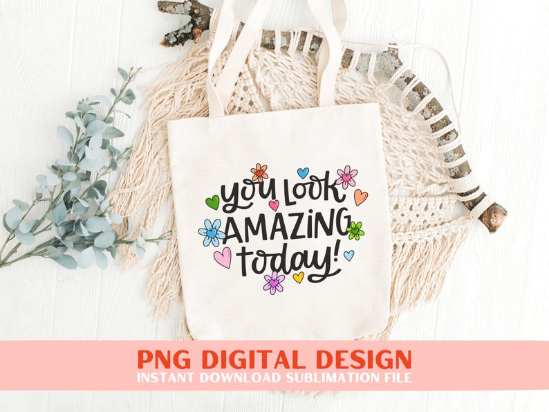 May include: A white tote bag featuring the text "you look amazing today!" in black lettering, surrounded by colourful flowers and hearts.