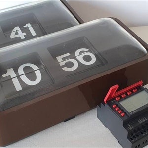 Puede incluir: Dos relojes de volteo marrones con cubiertas de plástico transparente que muestran la hora 9:41 y 10:56. Un temporizador digital negro con una palanca roja está en primer plano.