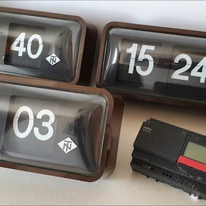 Puede incluir: Tres relojes de volteo vintage con caras negras y números blancos. Los relojes son de madera y tienen un frente de vidrio. Los relojes muestran las horas 9:40, 15:24 y 19:03. También hay un dispositivo electrónico negro y rojo en la imagen.