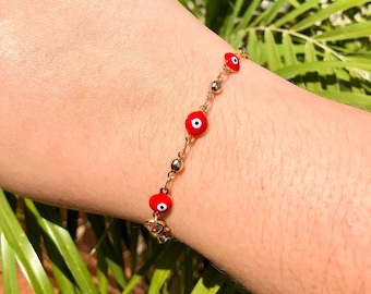 Puede incluir: Pulsera de cadena dorada con dijes de ojo turco rojo.