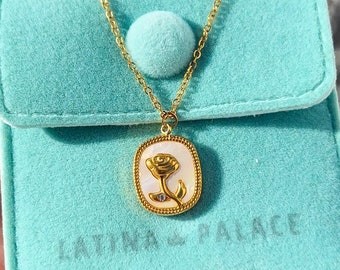 Peut inclure: Un collier en chaîne dorée avec un pendentif ovale blanc orné d'une rose dorée. Le collier est dans une pochette en velours bleu clair avec le texte "LATINA PALACE".