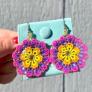 K&ouml;nnte beinhalten: Ein Paar Perlenohrringe mit Blumenmuster. Die Ohrringe sind rosa, lila und gelb.