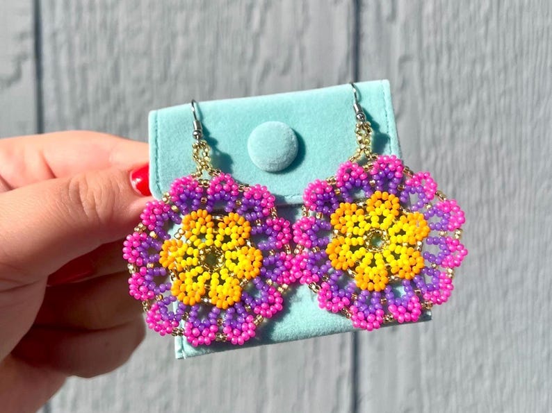K&ouml;nnte beinhalten: Ein Paar Perlenohrringe mit Blumenmuster. Die Ohrringe sind rosa, lila und gelb.