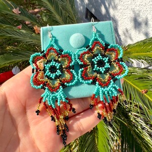 May include: A pair of turquoise, red, gold, and black beaded earrings with a flower design and dangling fringe.