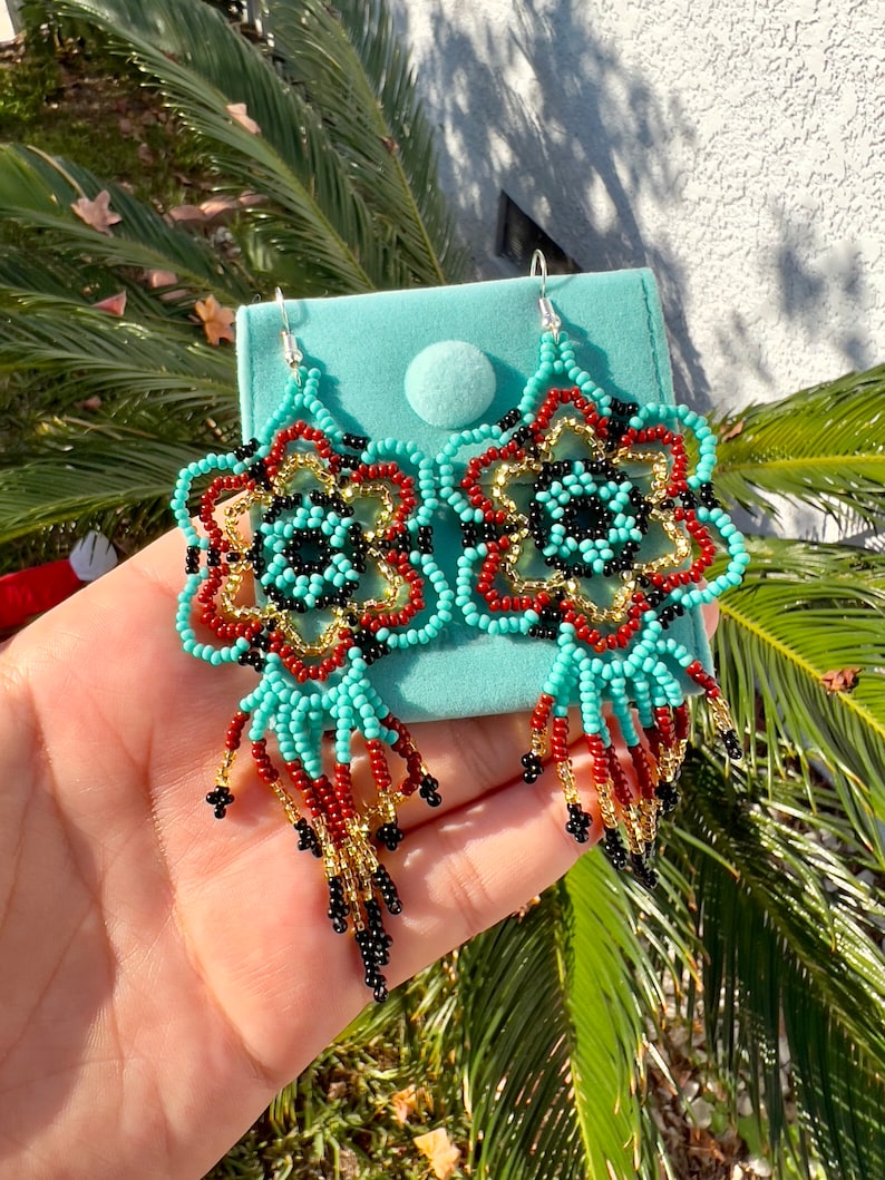 May include: A pair of turquoise, red, gold, and black beaded earrings with a flower design and dangling fringe.