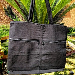 May include: Black canvas tote bag with two zippered pockets on the front. The bag has a black fabric handle.