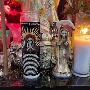 May include: A black and white candle with an image of Santa Muerte, a female skeletal figure, holding a rosary. The candle is labeled "Invocation of Santa Muerte". The text on the candle reads "Beautiful Death, beautiful Skeletal Saint, very Powerful and Strong, indispensable in the moment of danger, because I am sure of your greatness, I ask that you make immediately for those who have hurt me, all evil eye and bad intentions, make them feel the power of your wrath, I ask that you make them repent at my feet, Goddess Death, my Guardian Angel, I love you."