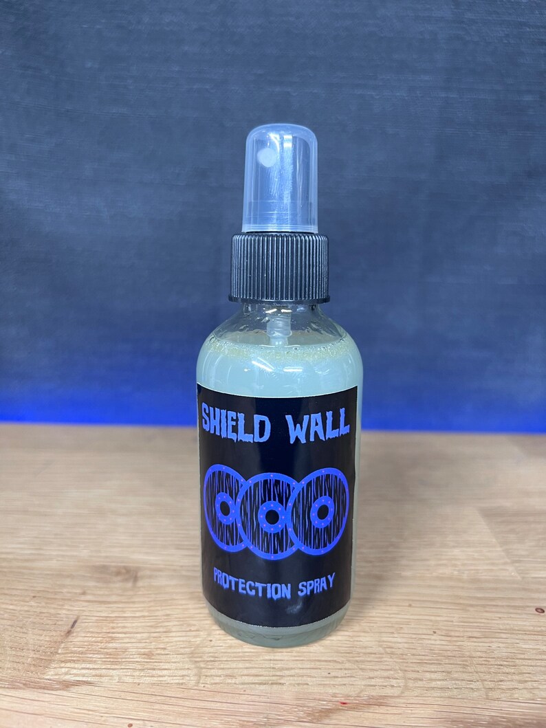 May include: A clear glass bottle with a black spray top and a black label that says "SHIELD WALL PROTECTION SPRAY". The label has a graphic of three blue interlocking circles with white dots.