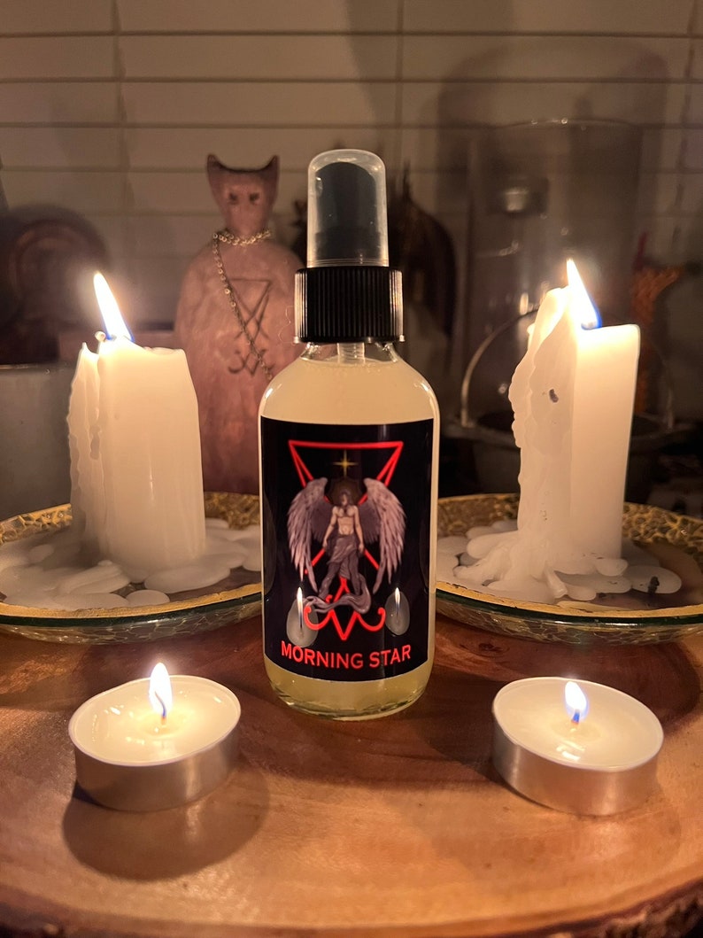 May include: A clear glass spray bottle with a black cap and a label featuring a winged figure and the words "MORNING STAR". The bottle is surrounded by lit candles and a statue.