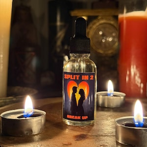 May include: A clear glass bottle with a black dropper, labelled "SPLIT IN 2 BREAK UP." The label shows a silhouette of a couple. The bottle is surrounded by lit candles, creating a dimly lit, intimate setting.