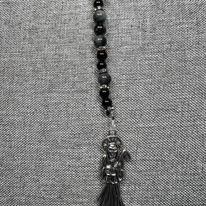 May include: A silver charm necklace with a black and grey beaded chain. The charm is a depiction of the Grim Reaper holding a scythe and a skull.