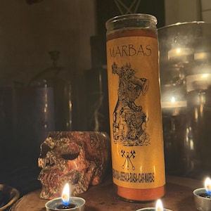 K&ouml;nnte beinhalten: Eine gelbe Kerze mit einem schwarzen Etikett, auf dem "MARBAS" steht, und einer Schwarzwei&szlig;illustration eines D&auml;mons, der eine Trompete h&auml;lt. Die Kerze ist von drei brennenden Teelichtern auf einer Holzoberfl&auml;che umgeben.