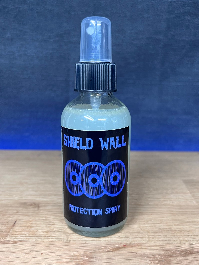 May include: A clear glass bottle with a black spray nozzle and a black label. The label says "Shield Wall" and features three blue and white shields with a white background. The label also says "Protection Spray".
