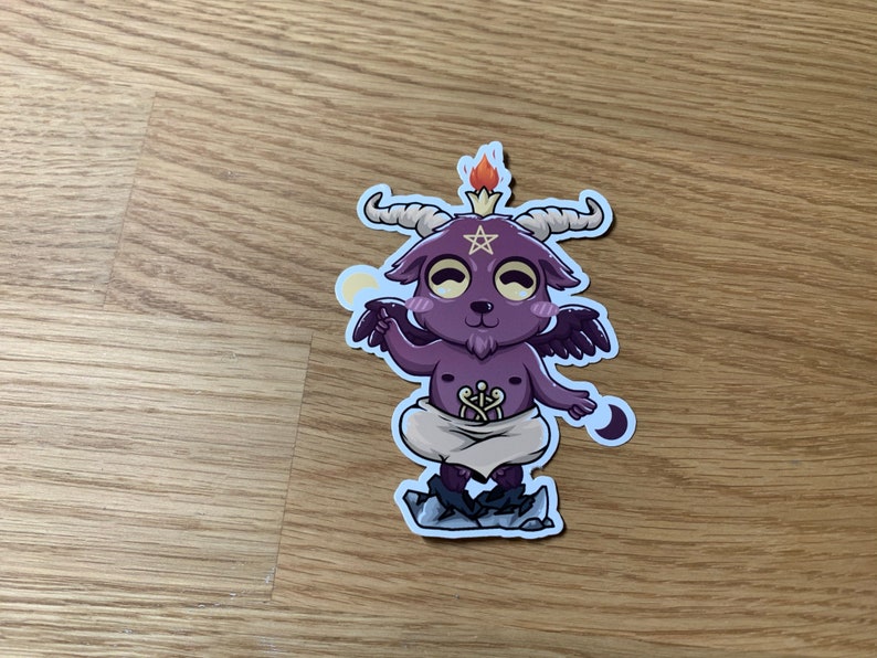 Pu&ograve; includere: Un piccolo diavolo di cartone animato viola con corna, ali e un pentagramma sulla testa. Il diavolo &egrave; in piedi su una roccia con una piccola fiamma sulla testa. Il diavolo indossa un pannolino bianco e ha un'espressione maliziosa sul viso.