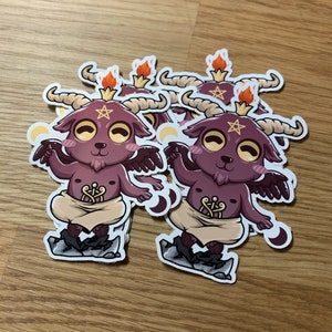 Pu&ograve; includere: Un set di cinque adesivi con un diavolo viola di cartone animato con corna, ali e un pentagramma sulla fronte. Il diavolo indossa un perizoma marrone e sta in piedi su una roccia. Gli adesivi sono stampati su carta bianca e hanno una finitura lucida.