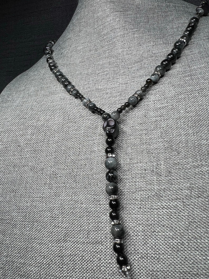 May include: A black and gray beaded necklace with a skull pendant. The beads are round and have a smooth, polished finish. The necklace is approximately 20 inches long.