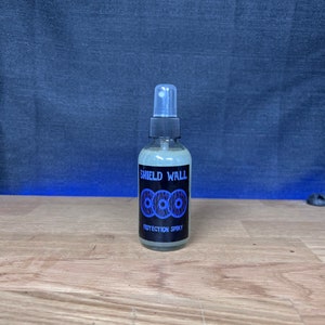 May include: A clear plastic bottle with a black spray nozzle and label. The label reads "Shield Wall Protection Spray" and features a blue and black logo of three interlocking circles.