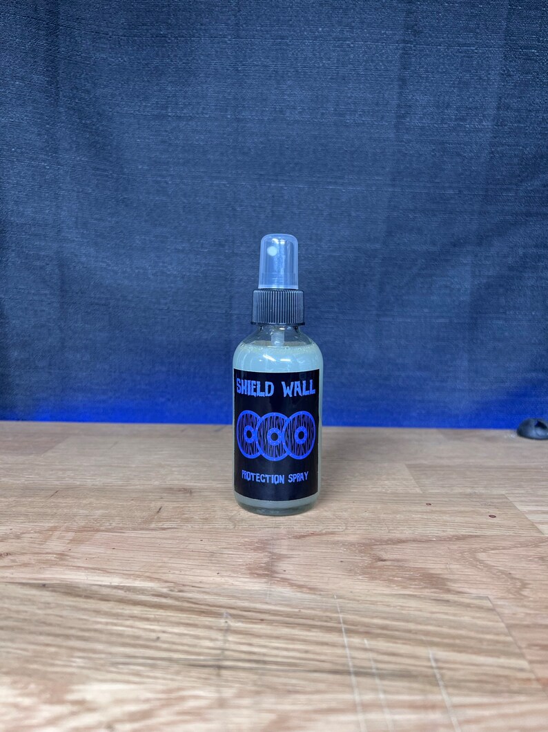 May include: A clear plastic bottle with a black spray nozzle and label. The label reads "Shield Wall Protection Spray" and features a blue and black logo of three interlocking circles.