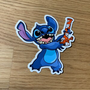 May include: A blue cartoon character with three fingers holding a red and white bong. The character has a wide grin and large, blue eyes.