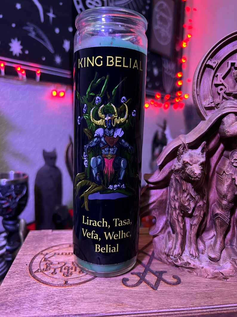 May include: A green glass candle with a black label. The label features a demon-like figure with a crown and a sword, surrounded by skulls. The text on the label reads "King Belial" and "Lirach, Tasa, Vefa, Welhc, Belial".