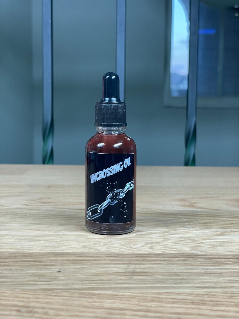 May include: A small brown glass bottle with a black dropper top. The bottle label is black with white text that reads "Uncrossing Oil" and a graphic of a broken chain.