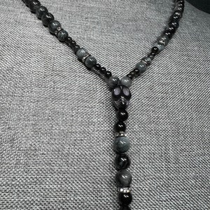 May include: A black and gray beaded necklace with a skull pendant. The beads are made of tiger's eye and onyx.