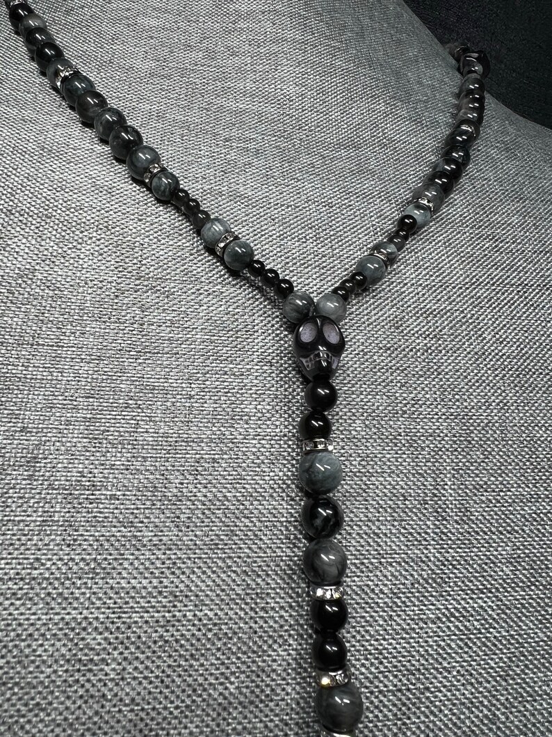 May include: A black and gray beaded necklace with a skull pendant. The beads are made of tiger's eye and onyx.