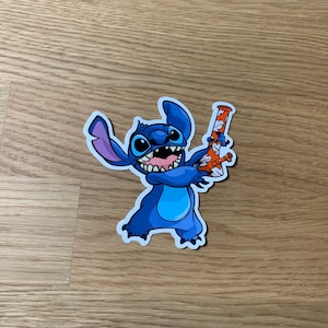 May include: A blue cartoon character with three fingers holding a glass bong with orange and white designs. The character has a big smile and is wearing a blue shirt.