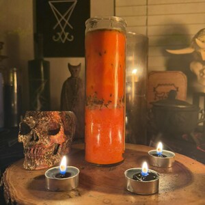 K&ouml;nnte beinhalten: Eine gro&szlig;e orangefarbene Kerze in einem Glasgef&auml;&szlig;, mit einem Sch&auml;del und drei brennenden Teelichtern auf einer Holzoberfl&auml;che.