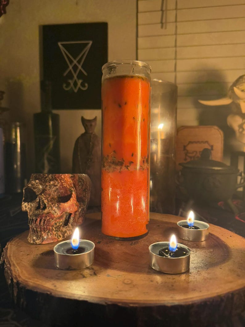 K&ouml;nnte beinhalten: Eine gro&szlig;e orangefarbene Kerze in einem Glasgef&auml;&szlig;, mit einem Sch&auml;del und drei brennenden Teelichtern auf einer Holzoberfl&auml;che.
