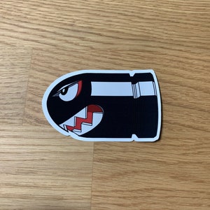 May include: Black and white sticker of a cartoon bullet bill with a red and white jagged tooth design.
