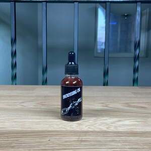 May include: A small, dark brown glass bottle with a black dropper top. The bottle has a black label with white text that reads "Uncrossing Oil" and a graphic of a chain breaking.