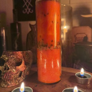 K&ouml;nnte beinhalten: Eine rote, orange und gr&uuml;ne, geschichtete Kerze in einem durchsichtigen Glasgef&auml;&szlig;. Die Kerze ist von drei Teelichtern auf einer Holzoberfl&auml;che umgeben.