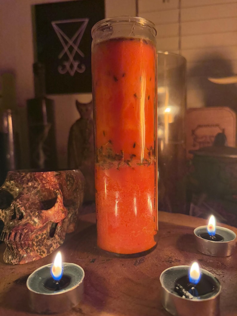 K&ouml;nnte beinhalten: Eine rote, orange und gr&uuml;ne, geschichtete Kerze in einem durchsichtigen Glasgef&auml;&szlig;. Die Kerze ist von drei Teelichtern auf einer Holzoberfl&auml;che umgeben.