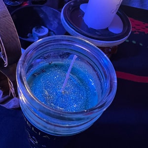 May include: A blue glass jar candle with a white wick and glitter. The candle is sitting on a dark blue surface.