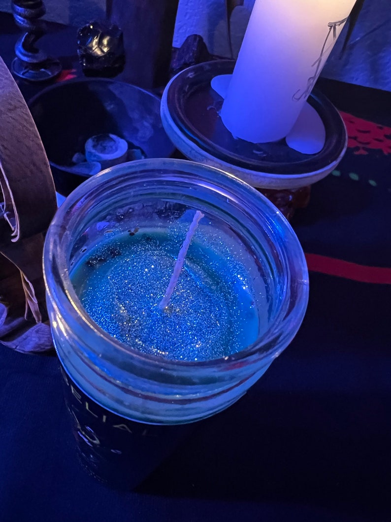 May include: A blue glass jar candle with a white wick and glitter. The candle is sitting on a dark blue surface.