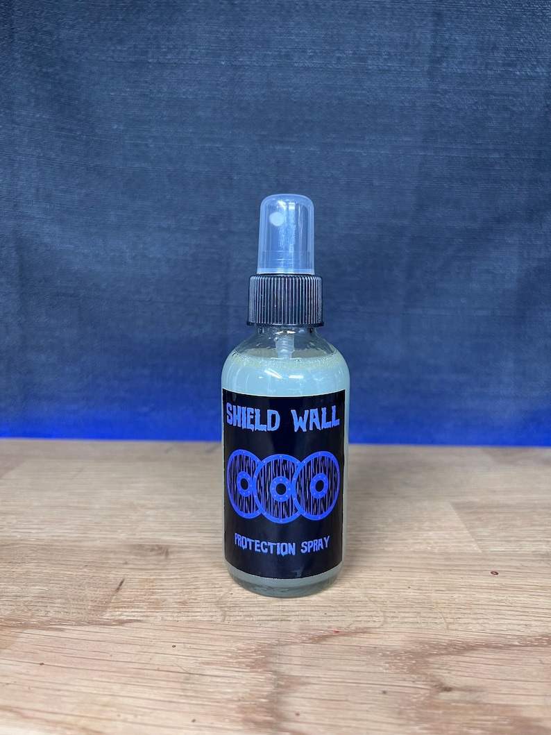 May include: A clear glass bottle with a black spray nozzle and a black label that says "Shield Wall Protection Spray". The label has a design of three blue circles with black outlines.