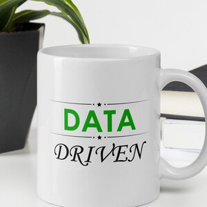 Peut inclure: Une tasse en céramique blanche avec un motif noir et vert. Le texte sur la tasse est "DATA DRIVEN".