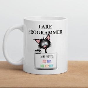 Op de afbeelding: Witte keramische mok met een zwarte kattenafbeelding en de tekst "I ARE PROGRAMMER". Daaronder een computertekening met de tekst "I MAKE COMPUTER" en "BEEP BOOP" in blauw, groen en rood.