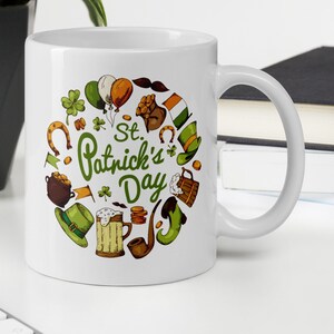 May include: White ceramic mug with a green, orange, and brown illustration of St. Patrick's Day themed icons, including a shamrock, a pot of gold, a leprechaun hat, and a beer mug. The text "St. Patrick's Day" is written in green.
