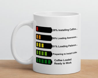 Op de afbeelding: Een witte keramische mok met een zwarte en groene voortgangsbalkgrafiek. De grafiek toont de voortgang van cafeïne, bewustzijn, geduld en koffie-installatie. De tekst luidt "28% Installing Caffine... 50% Loading Awereness... 81% Loading Patience... Preparing to Install Coffee Coffee Loaded Ready to Work"