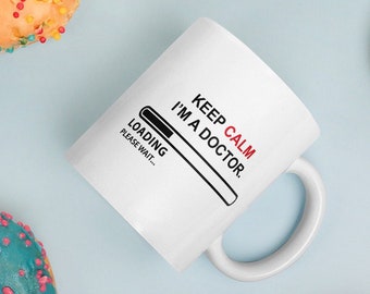 Op de afbeelding: Een witte keramische mok met een zwarte en rode afbeelding waarop staat "Keep Calm I'm a Doctor." De afbeelding bevat een voortgangsbalk met de tekst "Loading... Please Wait..."