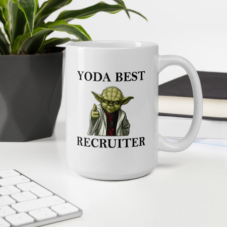 Pu&ograve; includere: Una tazza in ceramica bianca con un personaggio verde di Yoda che punta verso lo spettatore. Il testo "YODA BEST RECRUITER" &egrave; stampato sulla tazza.