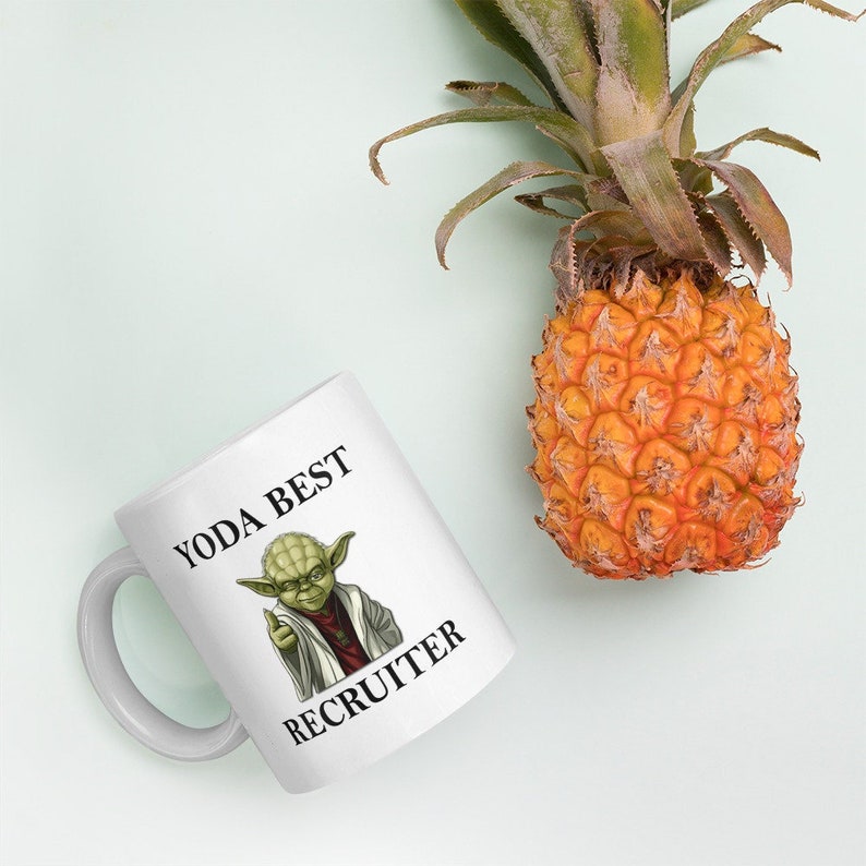 Pu&ograve; includere: Una tazza in ceramica bianca con un personaggio verde di Yoda e il testo "YODA BEST RECRUITER".