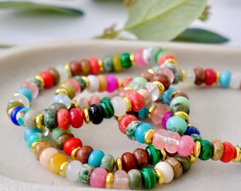 May include: A multi-strand bracelet featuring a variety of colorful gemstone beads in shades of red, green, blue, pink, yellow, and white, interspersed with small, polished gold-tone metal spacer beads arranged in a circular pattern.