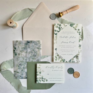 Puede incluir: Un conjunto de invitaciones de boda con un diseño de eucalipto en acuarela. La tarjeta de invitación incluye el texto "Están invitados a celebrar el matrimonio de Michelle Johns & James Reed" con la fecha y la ubicación. La tarjeta RSVP incluye el texto "Respondan amablemente antes del 3 de agosto de 2022" con opciones para aceptar o rechazar.